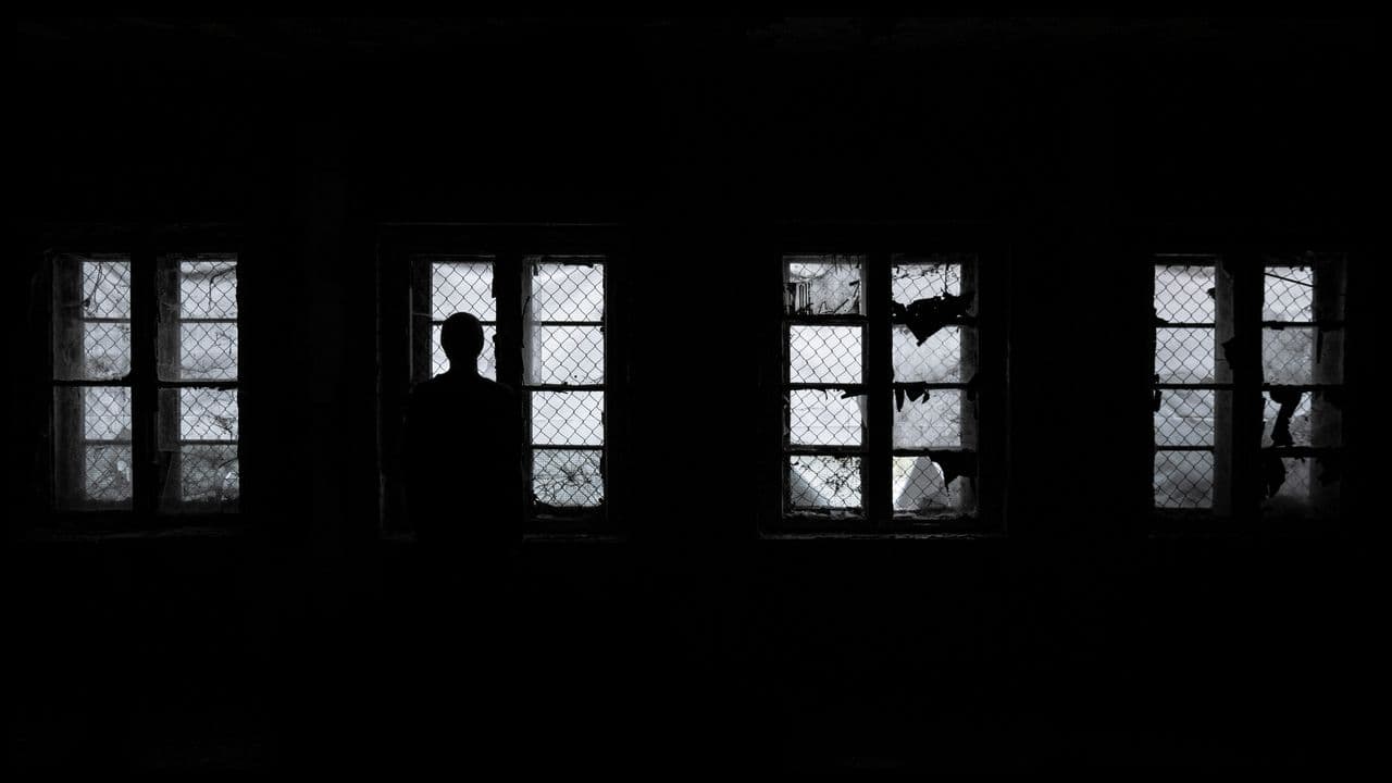 A black and white photo where the only light is coming in through broken windows and a person is standing in front of them