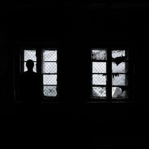 A black and white photo where the only light is coming in through broken windows and a person is standing in front of them